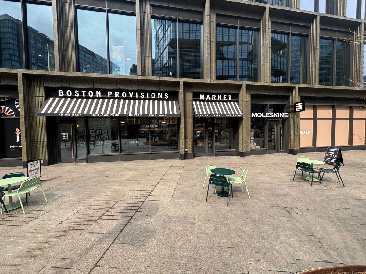The Boston Provisions Market storefront on Boston Wharf Road, with striped awnings beneath a finished concrete facade.